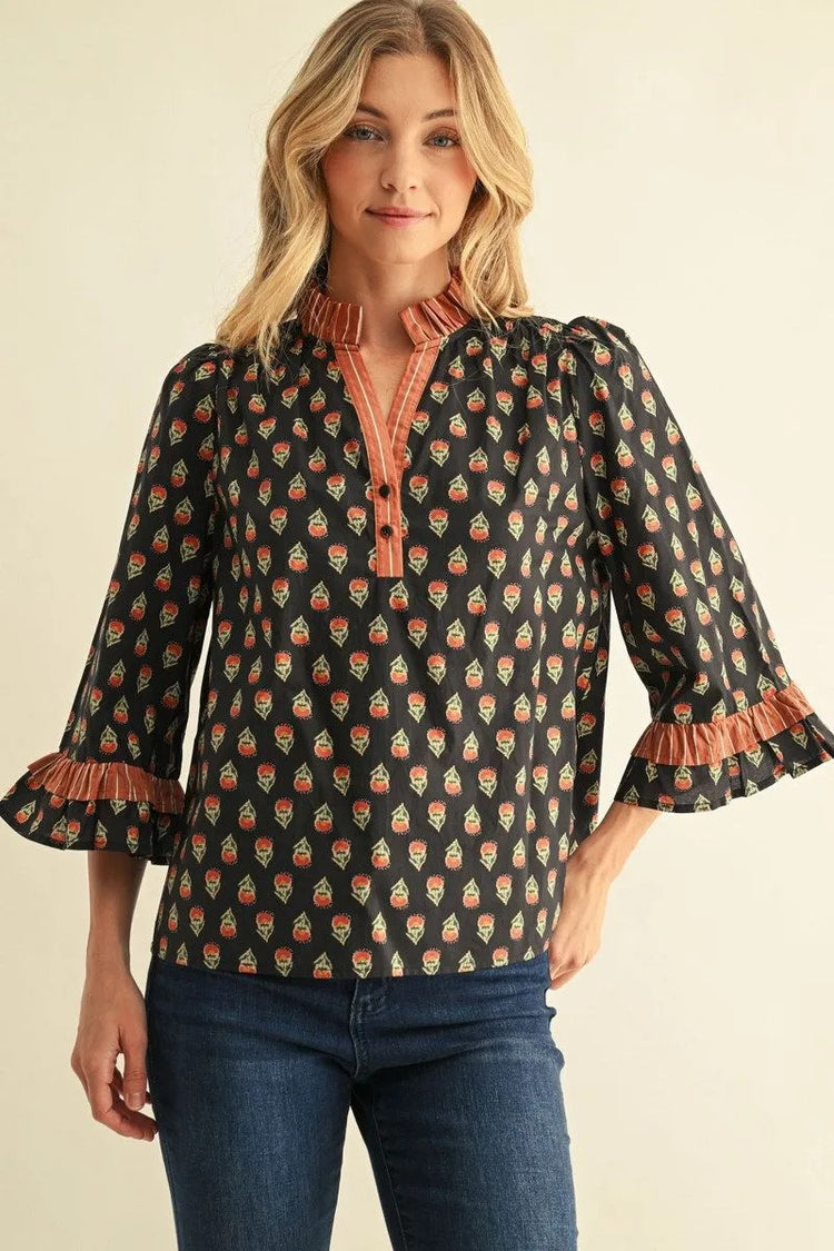 Woman wearing a black Jane floral top with 3/4 bell sleeves, ruffle neck, and stripe contrast trim.