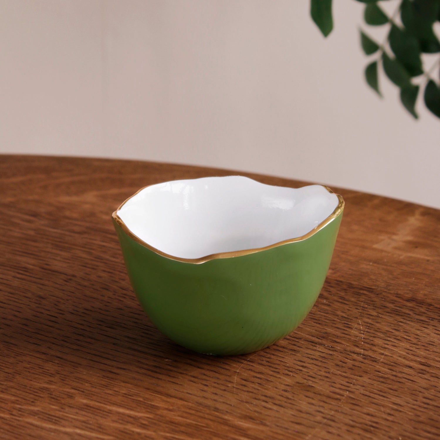 Encanto Osaka small bowl with a leaf green exterior, white interior, and gold rim on a wooden table.