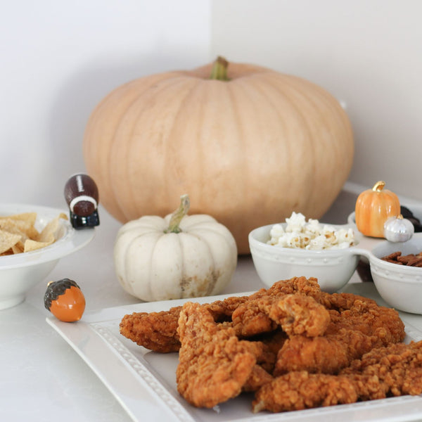 A fall-themed snack spread with fried chicken, popcorn, chips, and decorative pumpkin accents.