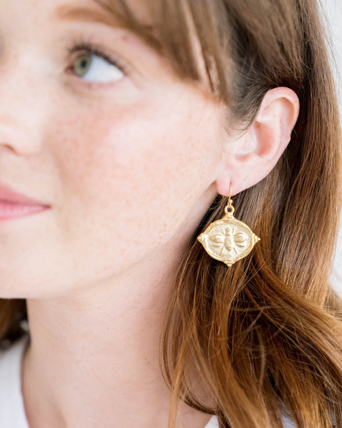 A woman wearing a gold bee intaglio earring with a fish hook back.