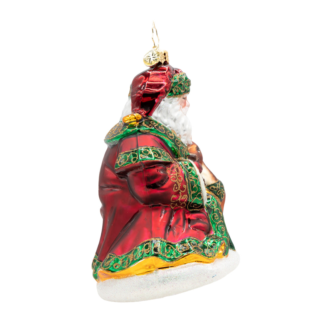 A Woodland Offering Santa glass ornament in a red robe with green and gold glitter details.