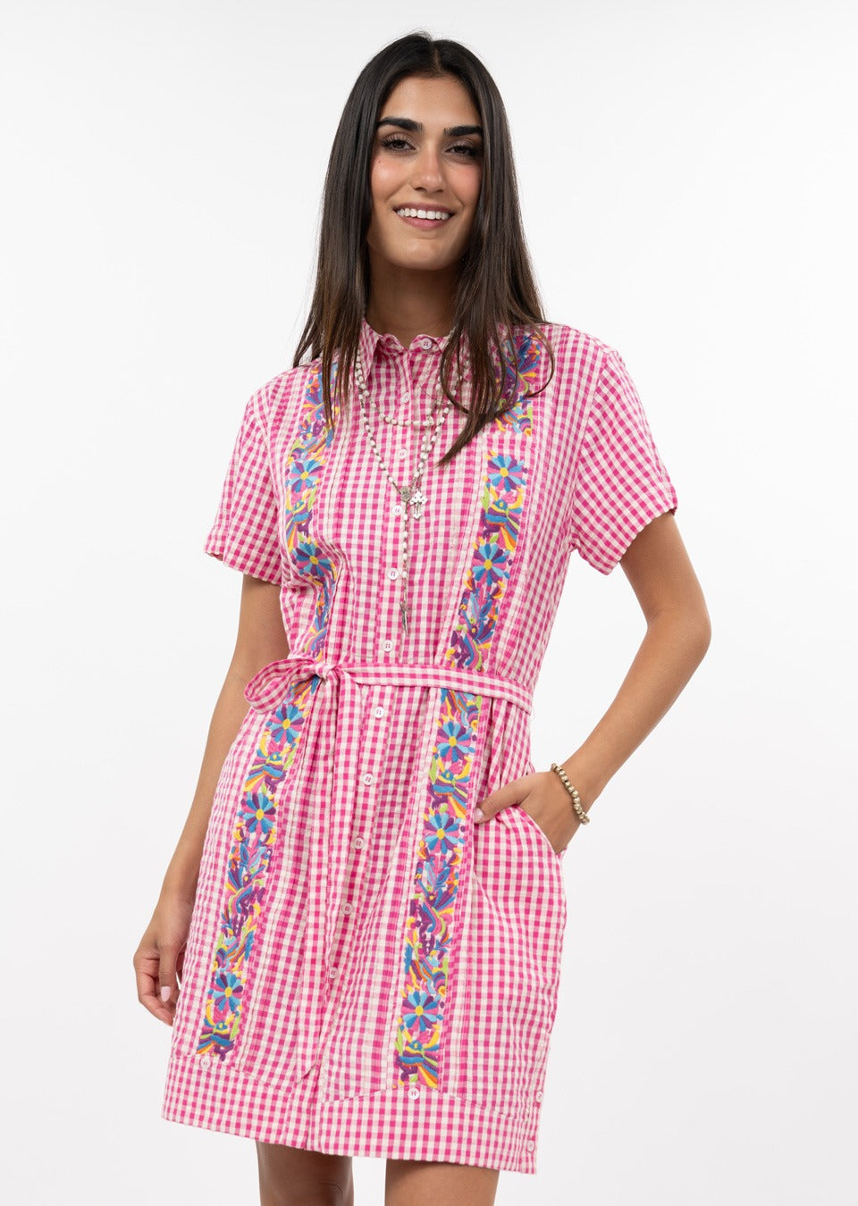 Woman wearing the Dominga Dress in pink and white gingham with colorful floral embroidery.
