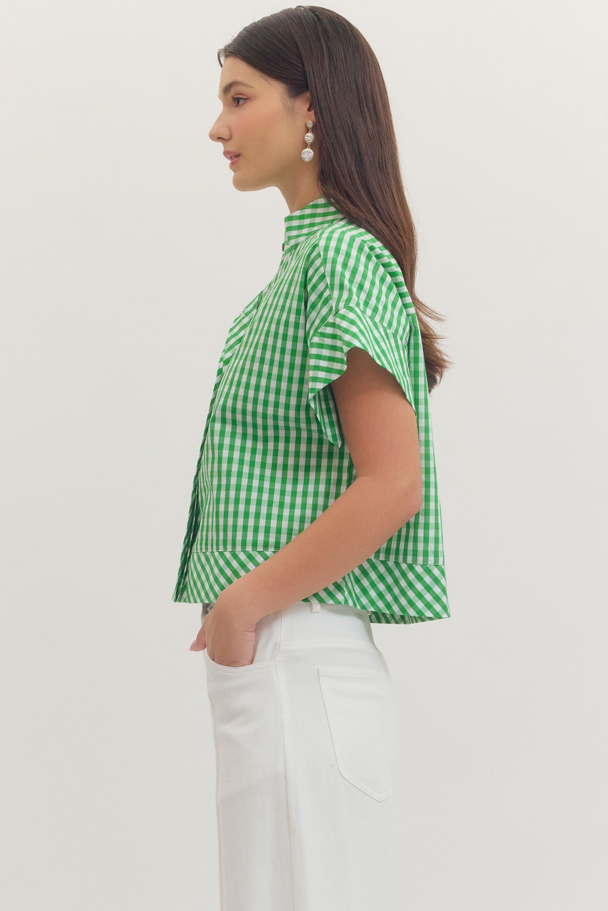 Side view of a woman wearing a green and white gingham print cap sleeve top and white pants.