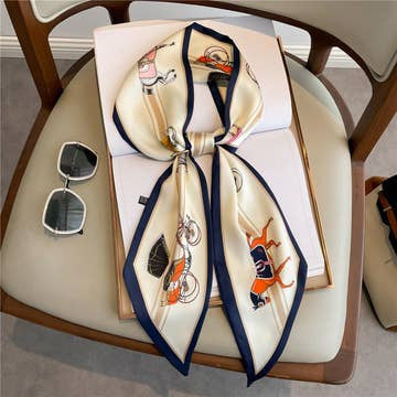 Beige thin bevel ribbon head scarf with horse print and navy border on a chair next to sunglasses.