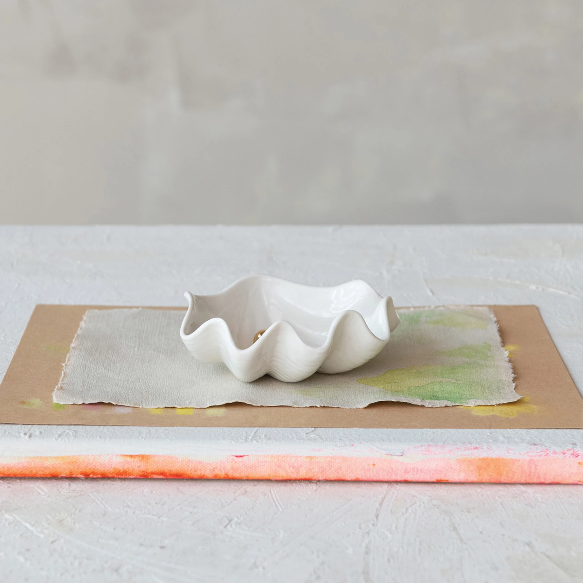 White stoneware clam shell shaped dish on a textured surface.