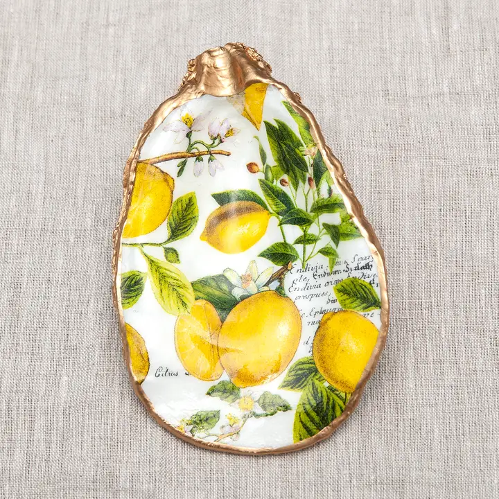 Decoupaged oyster shell with a lemon botanical print and metallic gold trim on a linen background.