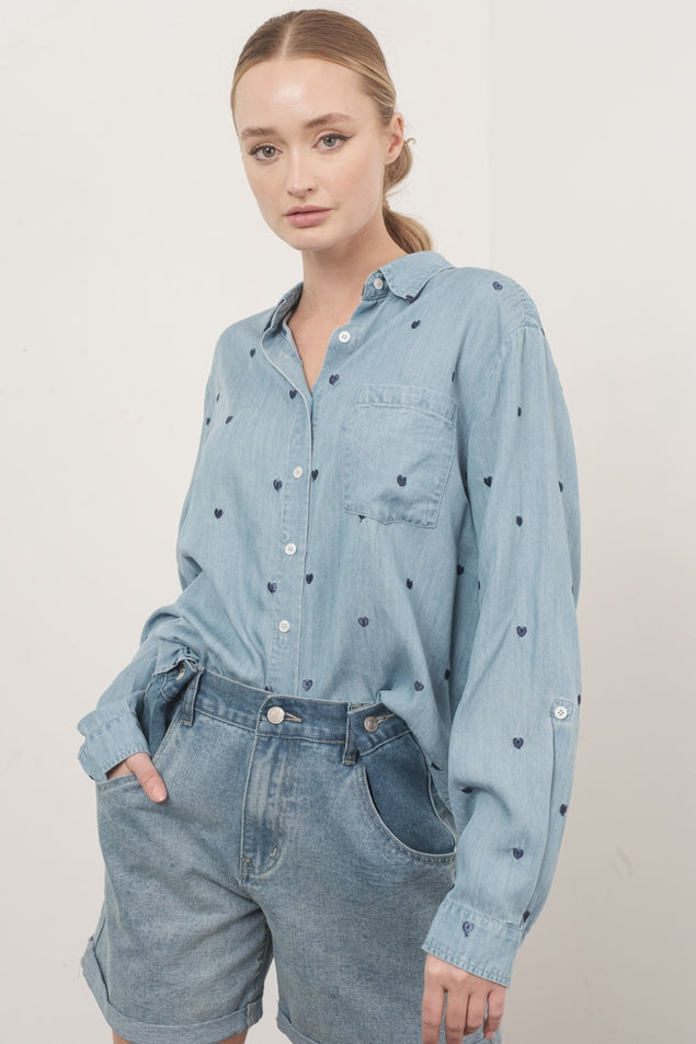 Woman wearing the Naomi Oversized Chambray Heart Shirt in light blue with dark heart embroidery.