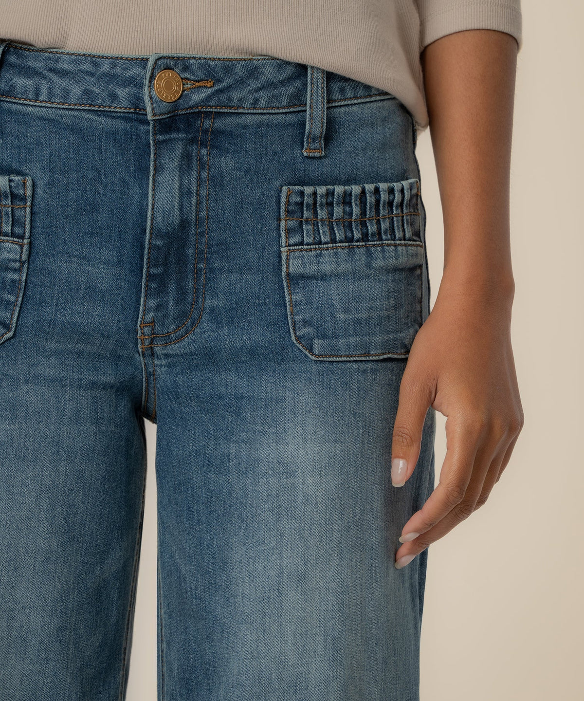 Close-up of high-rise wide-leg blue jeans featuring front patch pockets with ruched detailing.