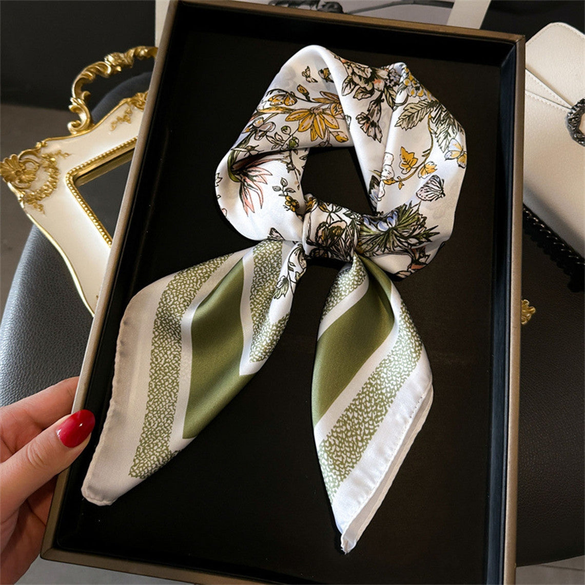 Silky white scarf with yellow butterfly and green striped patterns, tied in a knot on a black tray.