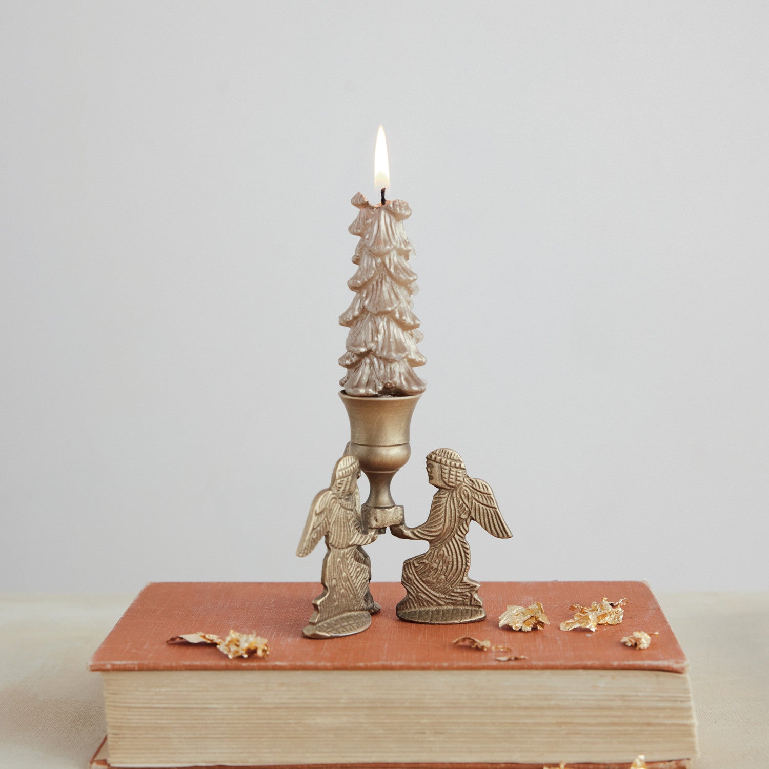 Gold finish metal taper holder featuring two kneeling angels supporting a lit tree-shaped candle.