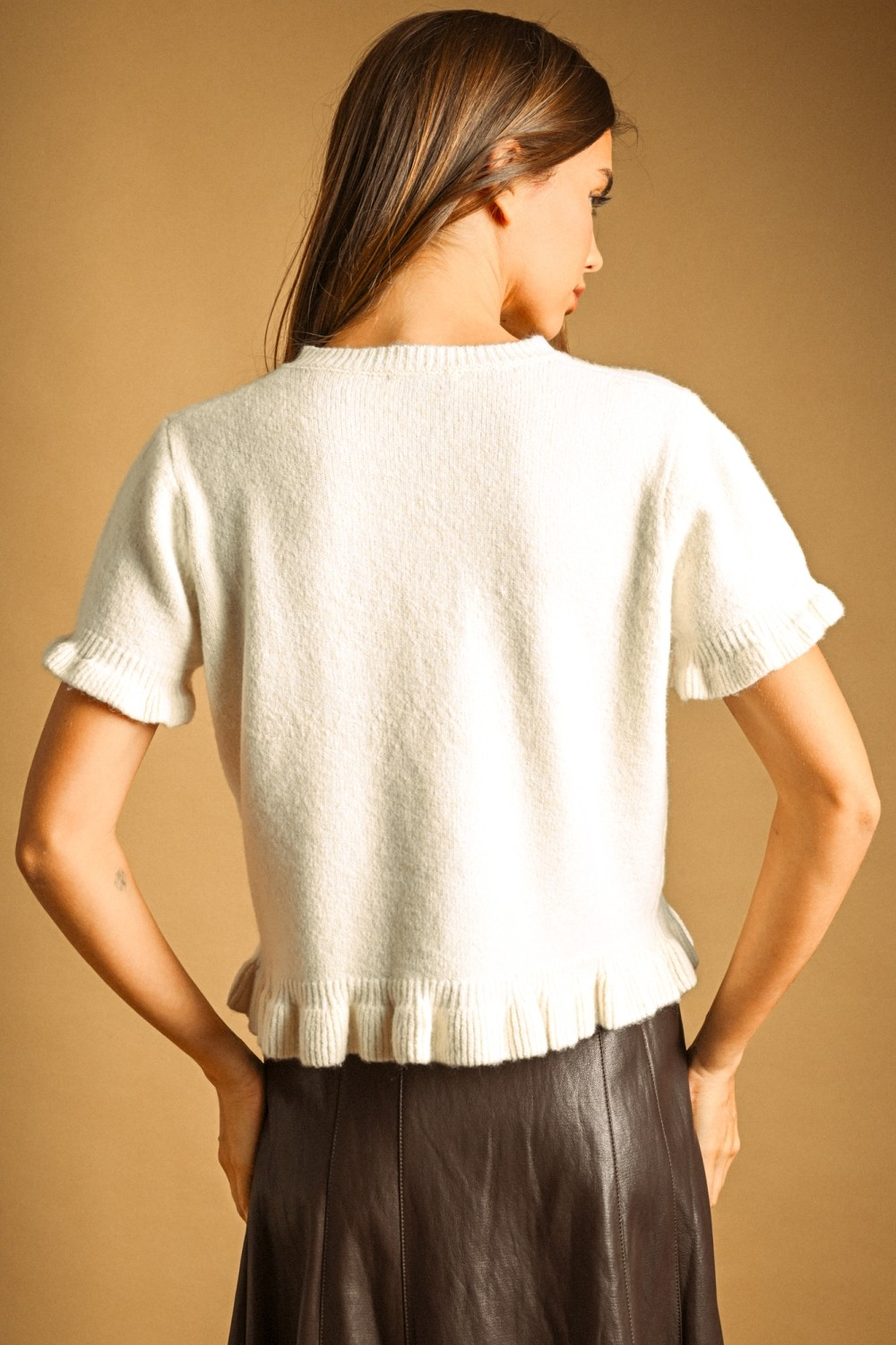 Back view of a woman wearing a white short sleeve sweater with a ribbed ruffle hem and cuffs.