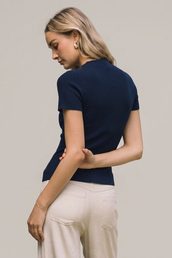 Back view of a woman wearing a navy blue short sleeve mock neck knit sweater top and beige pants.
