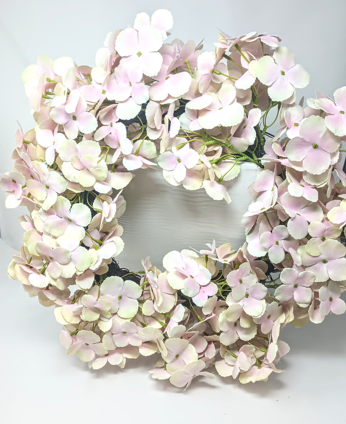 A round wreath made of polyester foam vines in white and soft pink hydrangea flowers.