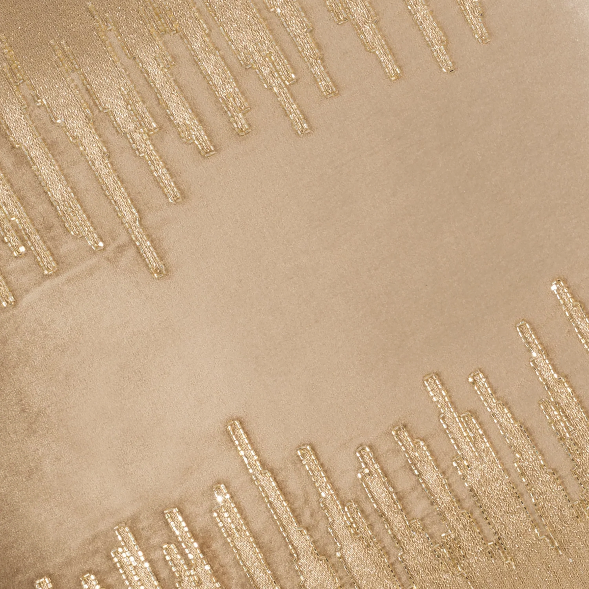 Close-up of a beige velvet pillow with gold beaded geometric patterns.