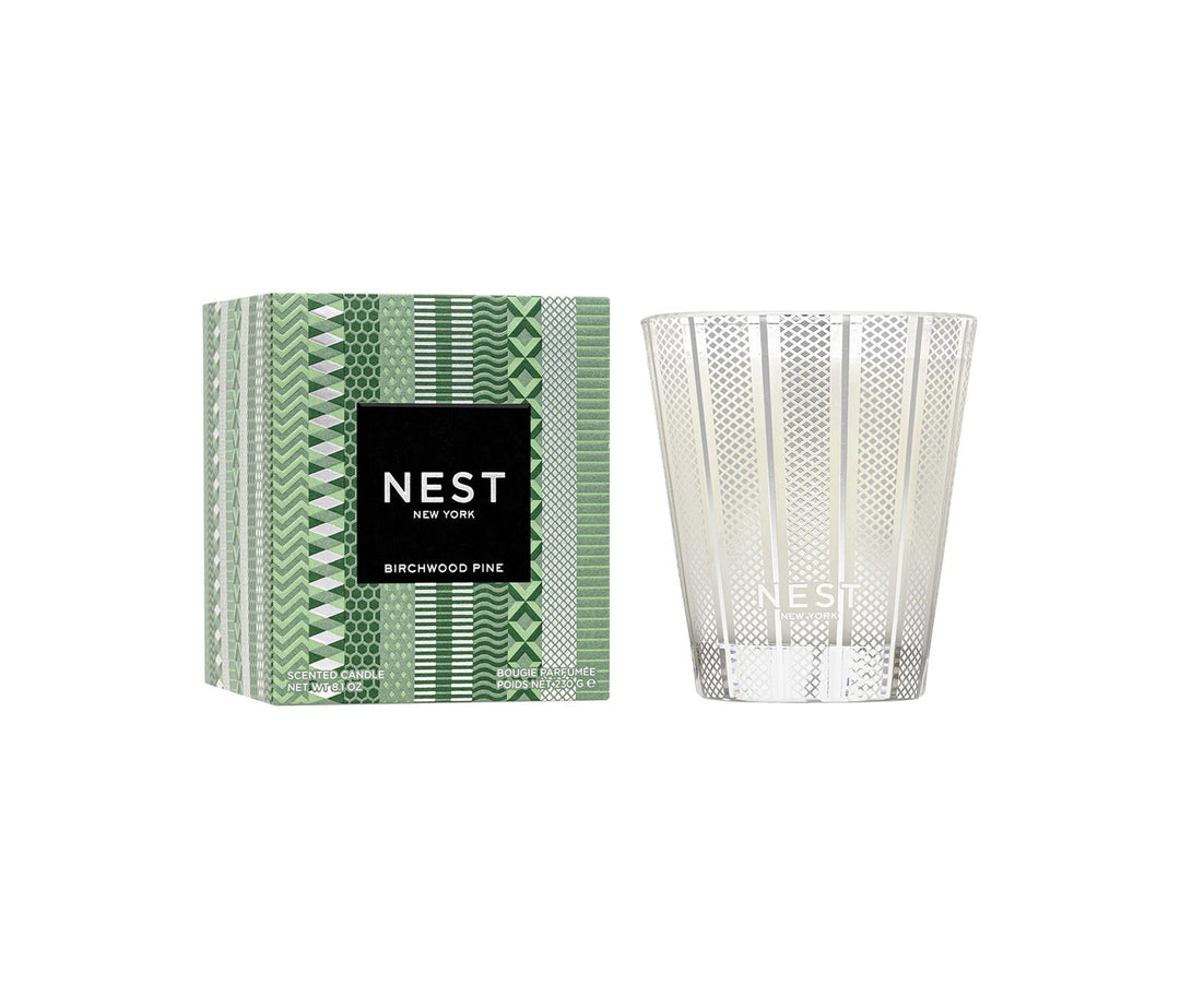 Nest Birchwood Pine Classic Candle in a silver patterned glass jar next to its green patterned box.