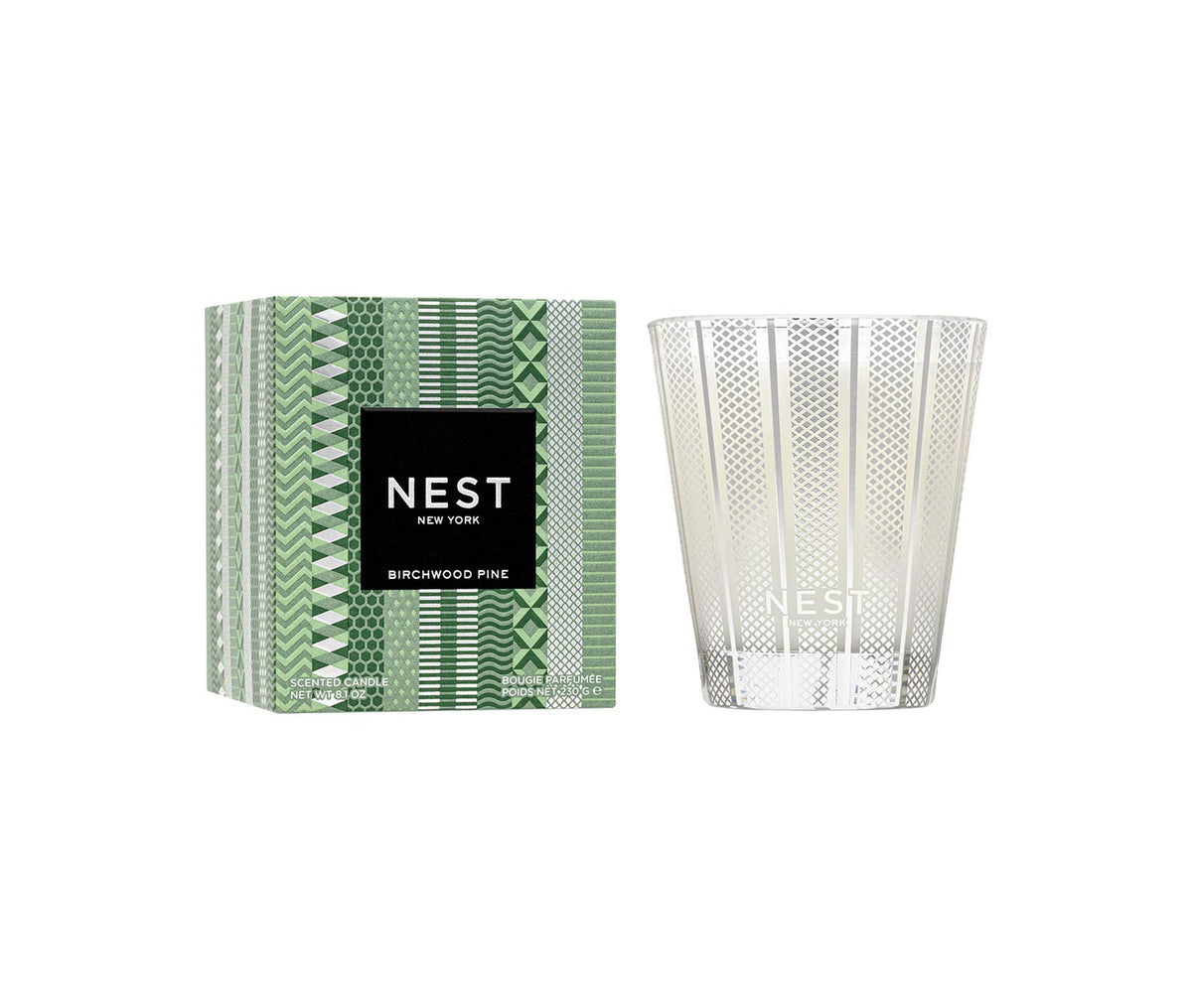 Nest Birchwood Pine Classic Candle in a silver patterned glass jar next to its green patterned box.