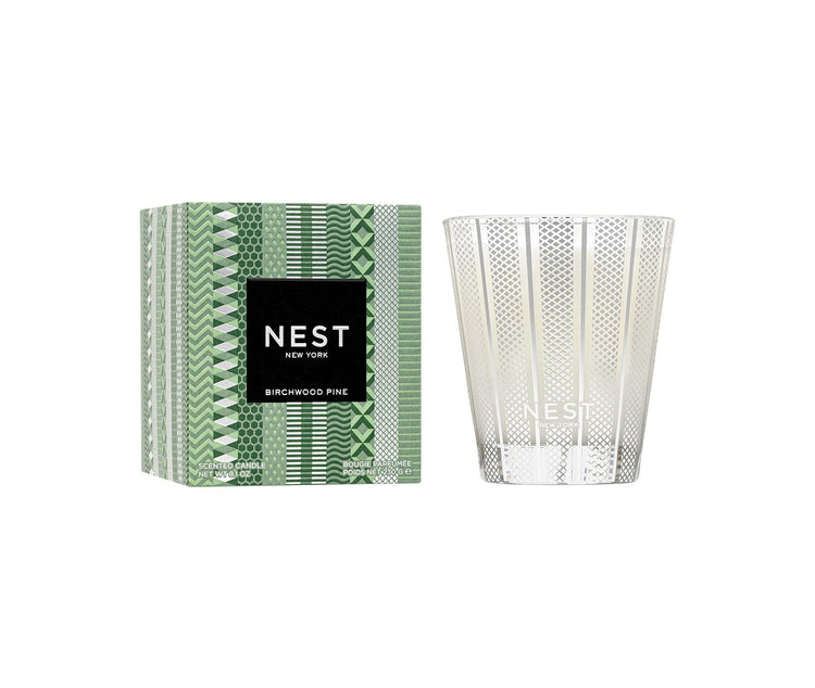Nest Birchwood Pine Classic Candle in a silver patterned glass jar next to its green patterned box.