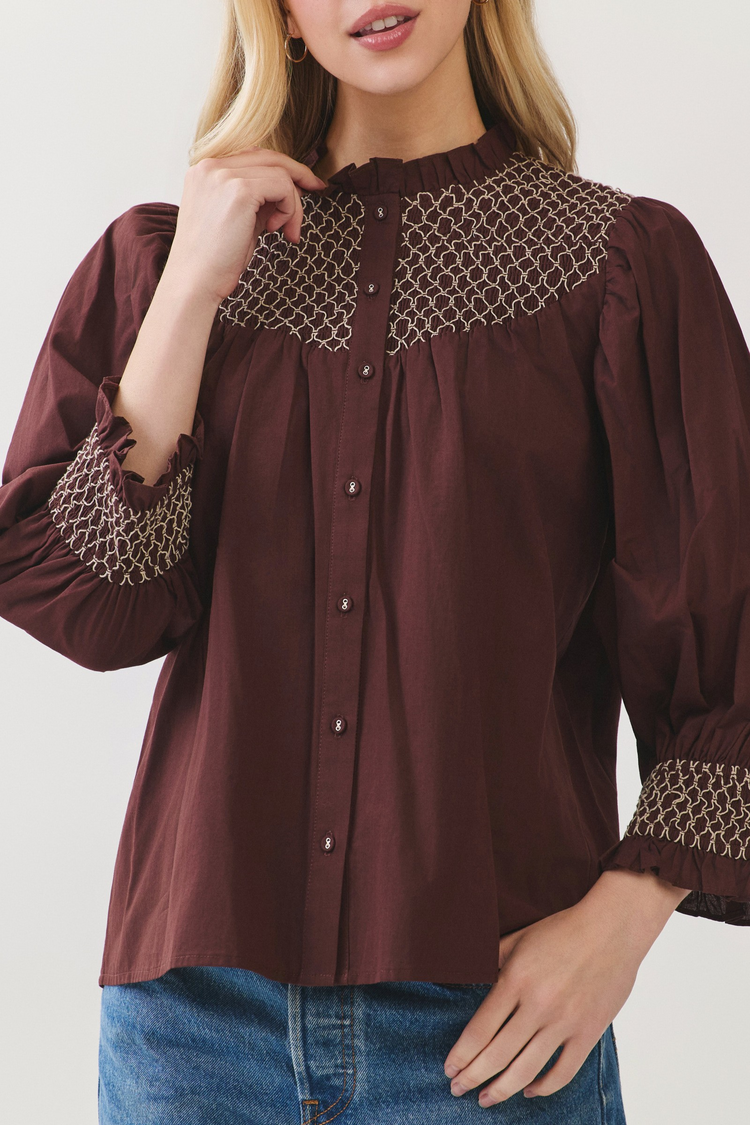 Woman wearing a Jenny burgundy cotton blouse with white embroidery on the yoke and ruffled cuffs.