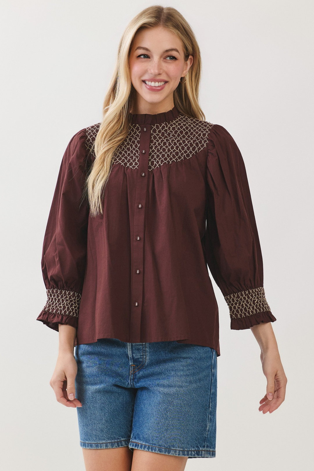 Woman wearing a Jenny Embroidered Button Down Blouse Top in burgundy with blue denim shorts.
