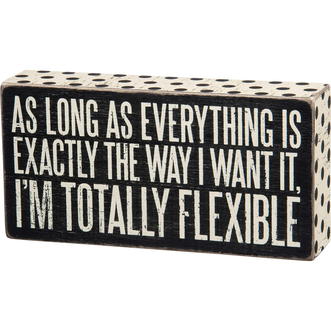 Black wooden box sign with white polka dots and text: "AS LONG AS EVERYTHING IS EXACTLY THE WAY I WANT IT, I'M TOTALLY FLEXIBLE."