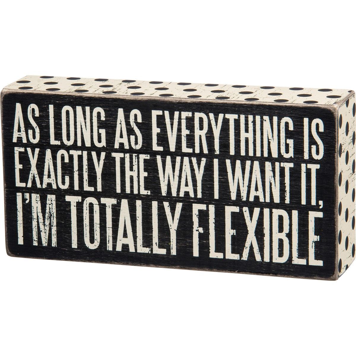 Black wooden box sign with white polka dots and text: "AS LONG AS EVERYTHING IS EXACTLY THE WAY I WANT IT, I'M TOTALLY FLEXIBLE."