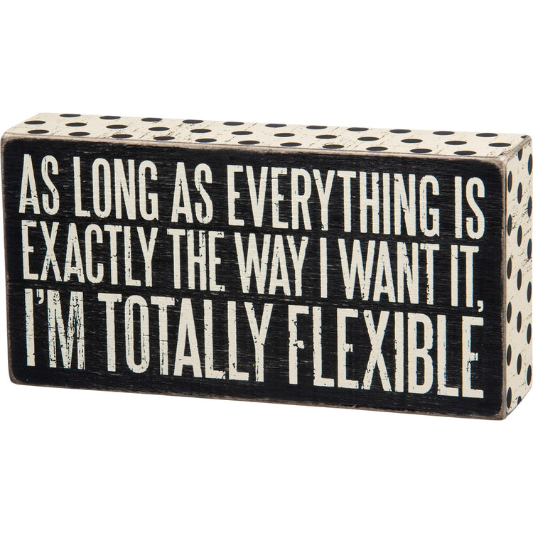Black wooden box sign with white polka dots and text: "AS LONG AS EVERYTHING IS EXACTLY THE WAY I WANT IT, I'M TOTALLY FLEXIBLE."