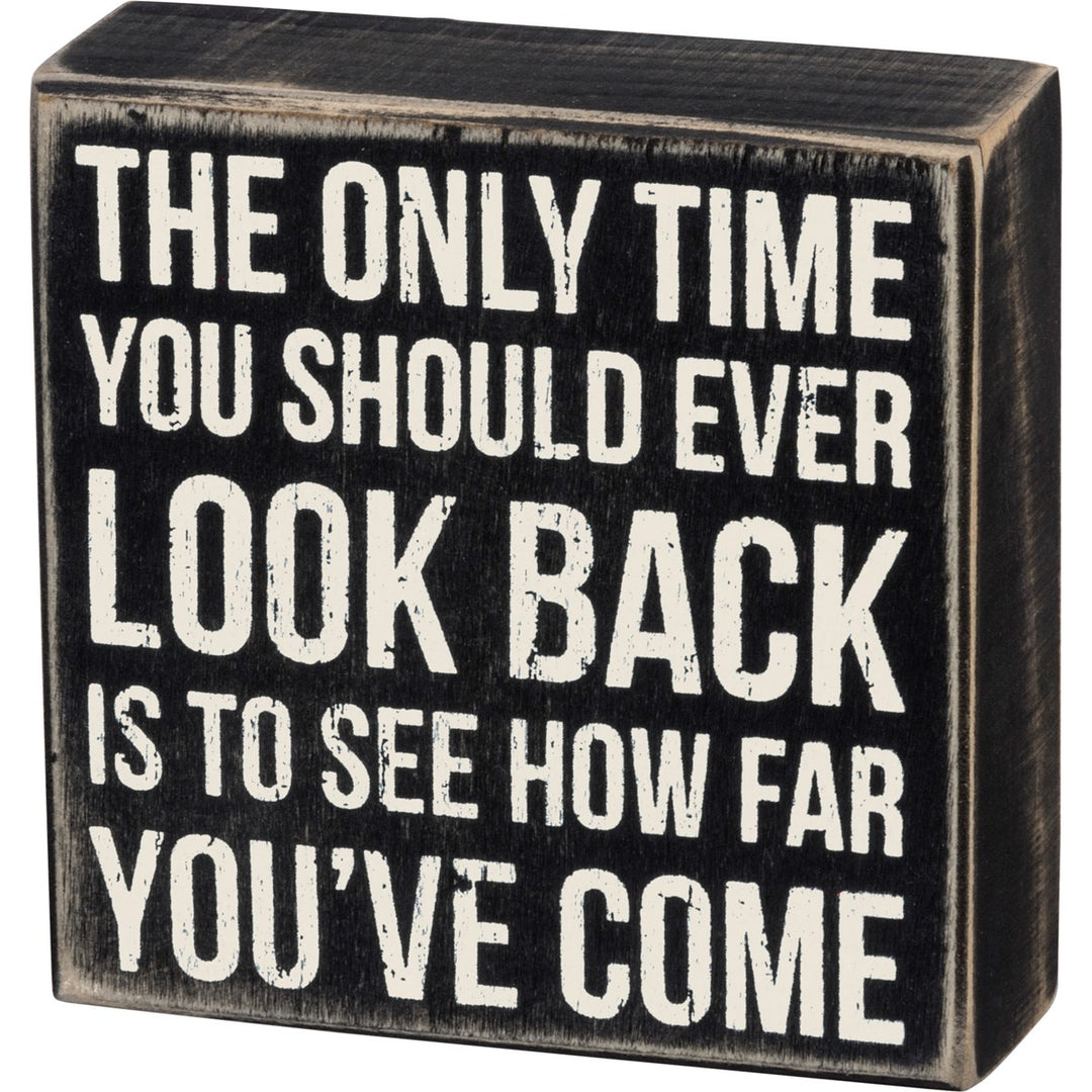 Black wooden box sign with white distressed text: "The only time you should ever look back is to see how far you've come."