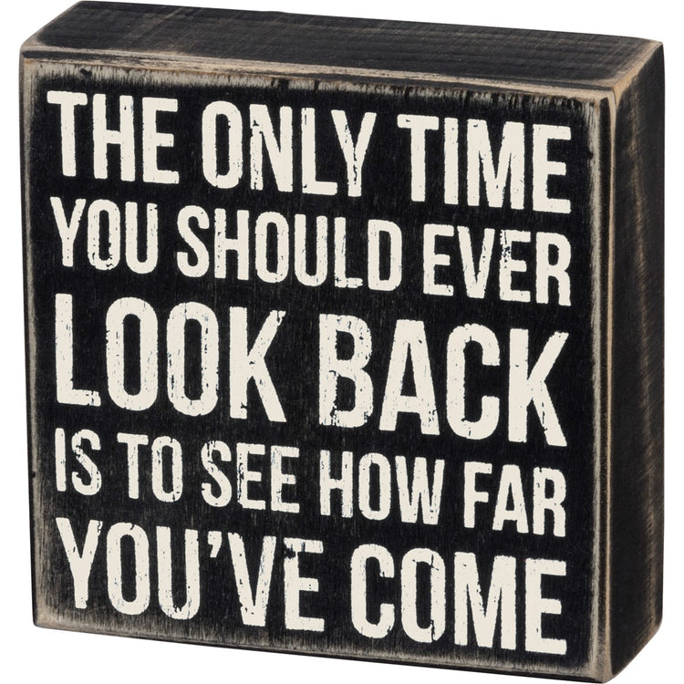 Black wooden box sign with white distressed text: "The only time you should ever look back is to see how far you've come."
