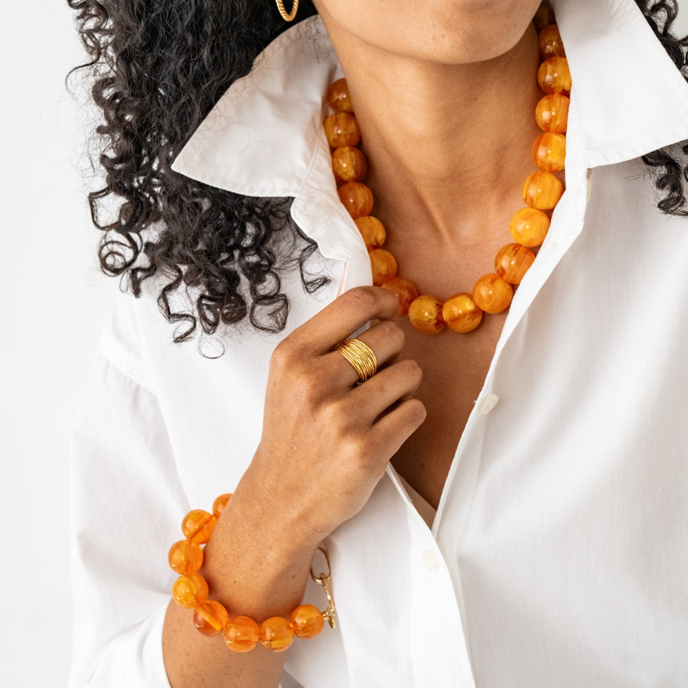A person wearing the Cece Large Resin Bead Bracelet in amber with a matching necklace.