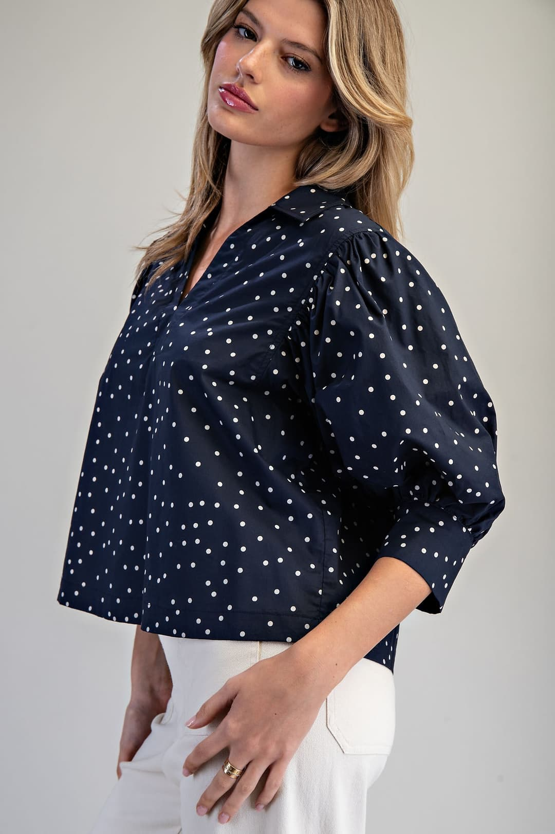 Woman wearing a navy blue Molly Polka Dot Puff Sleeve Blouse with white pants.