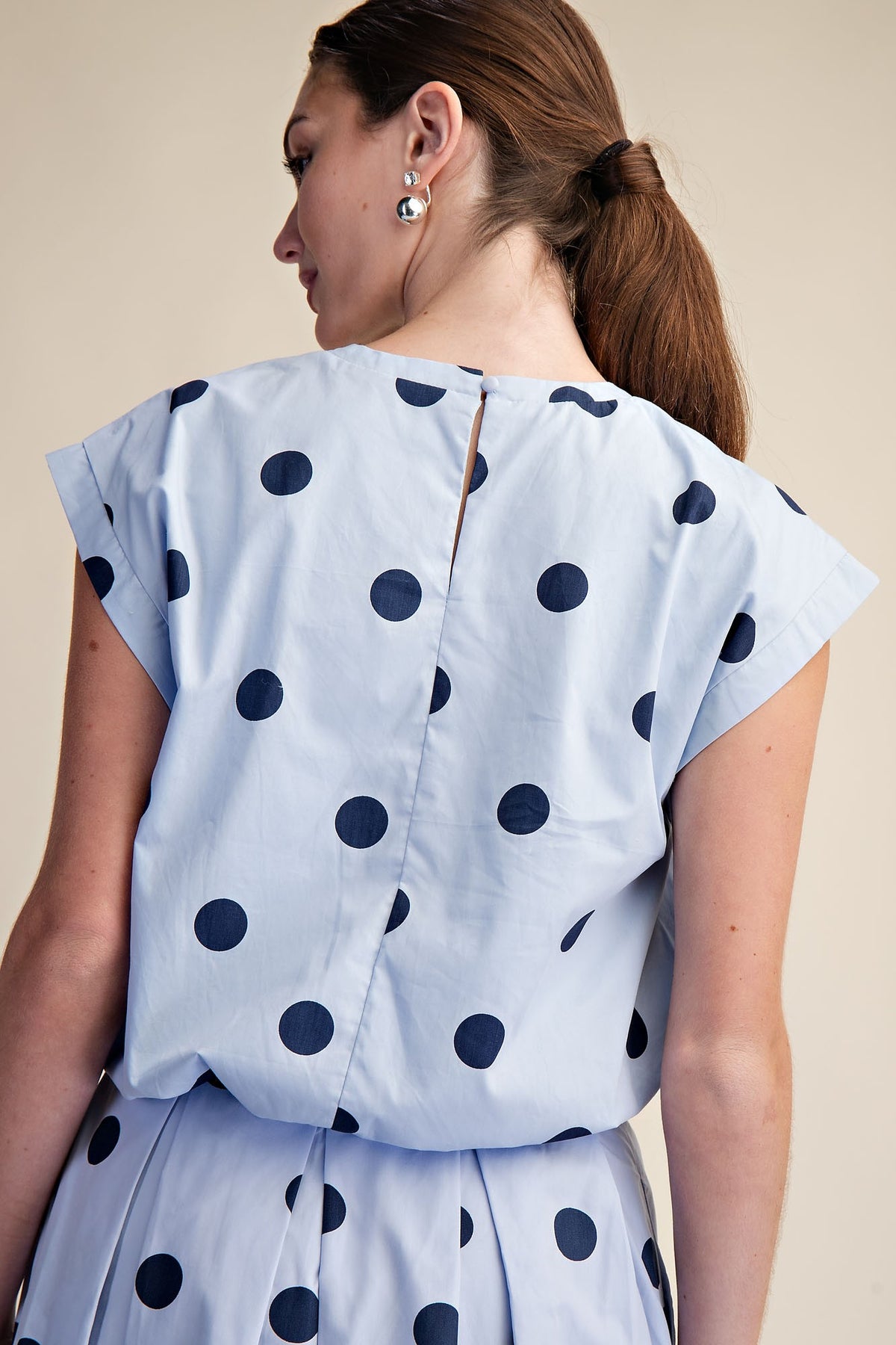 Back view of a light blue round neck bubble crop top with large navy blue polka dots.