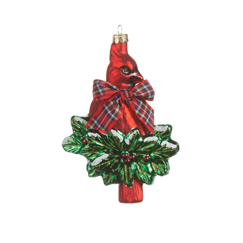 Glass cardinal ornament with a plaid bow perched on green holly leaves with red berries.