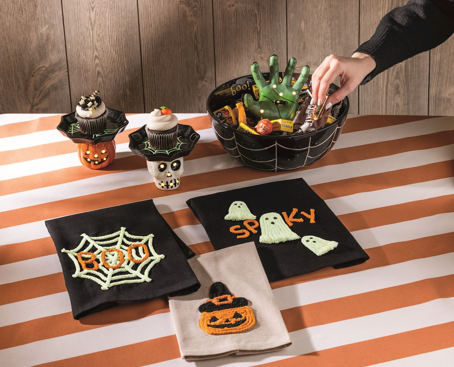 A black spiderweb bowl with a green light-up hand reaching out from a pile of Halloween candy.
