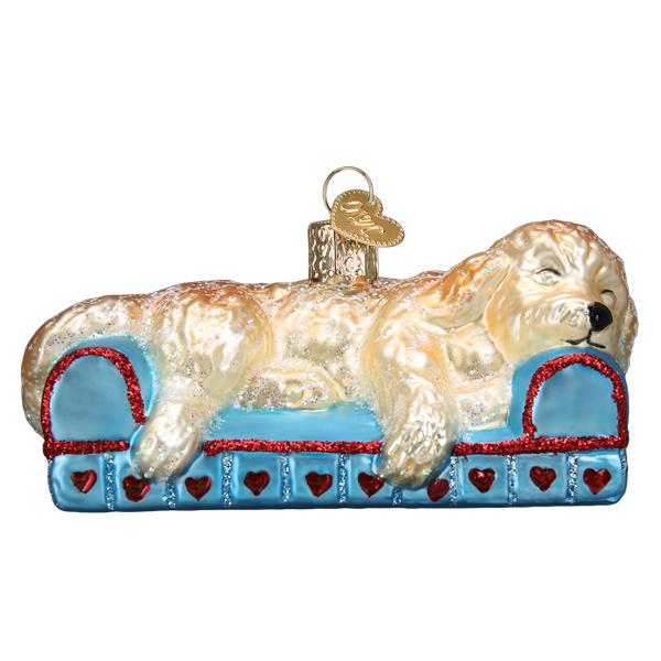 Glass Christmas ornament of a golden doodle dog sleeping on a blue sofa with red glitter hearts.