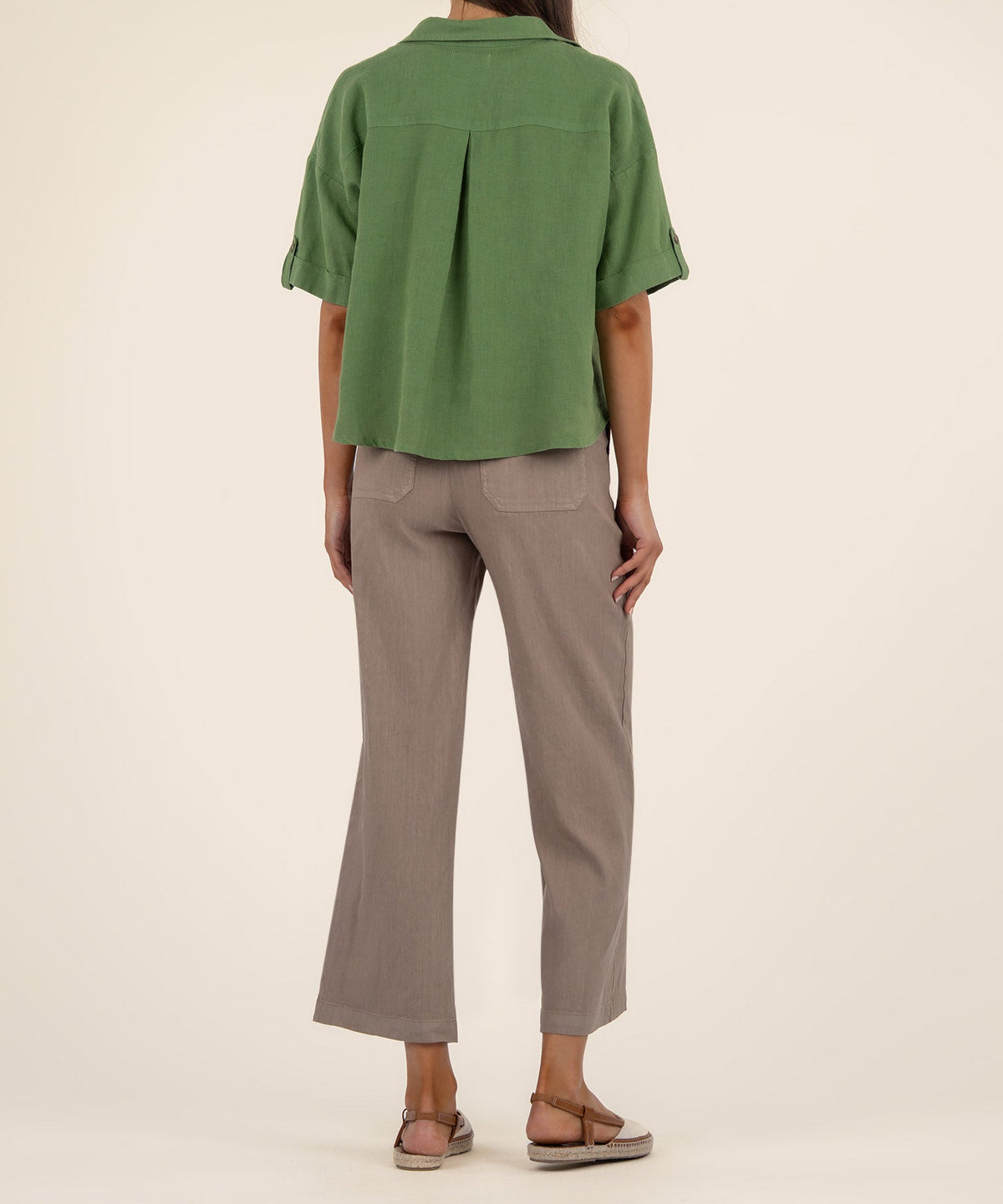 Back view of a woman wearing a green boxy short-sleeve linen shirt and taupe cropped pants.