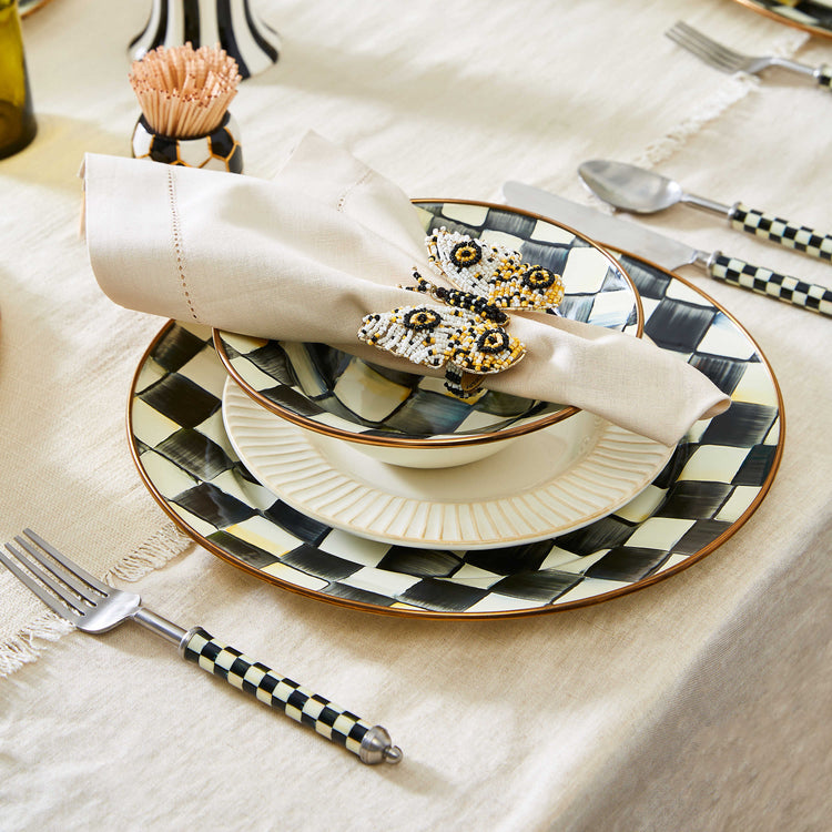 Hand-painted Courtly Check enamel charger plate on a table setting with a napkin and cutlery.