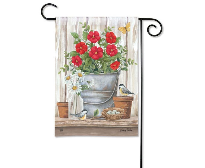 Garden flag with red flowers in a bucket, daisies, birds, and a butterfly on a wooden background.