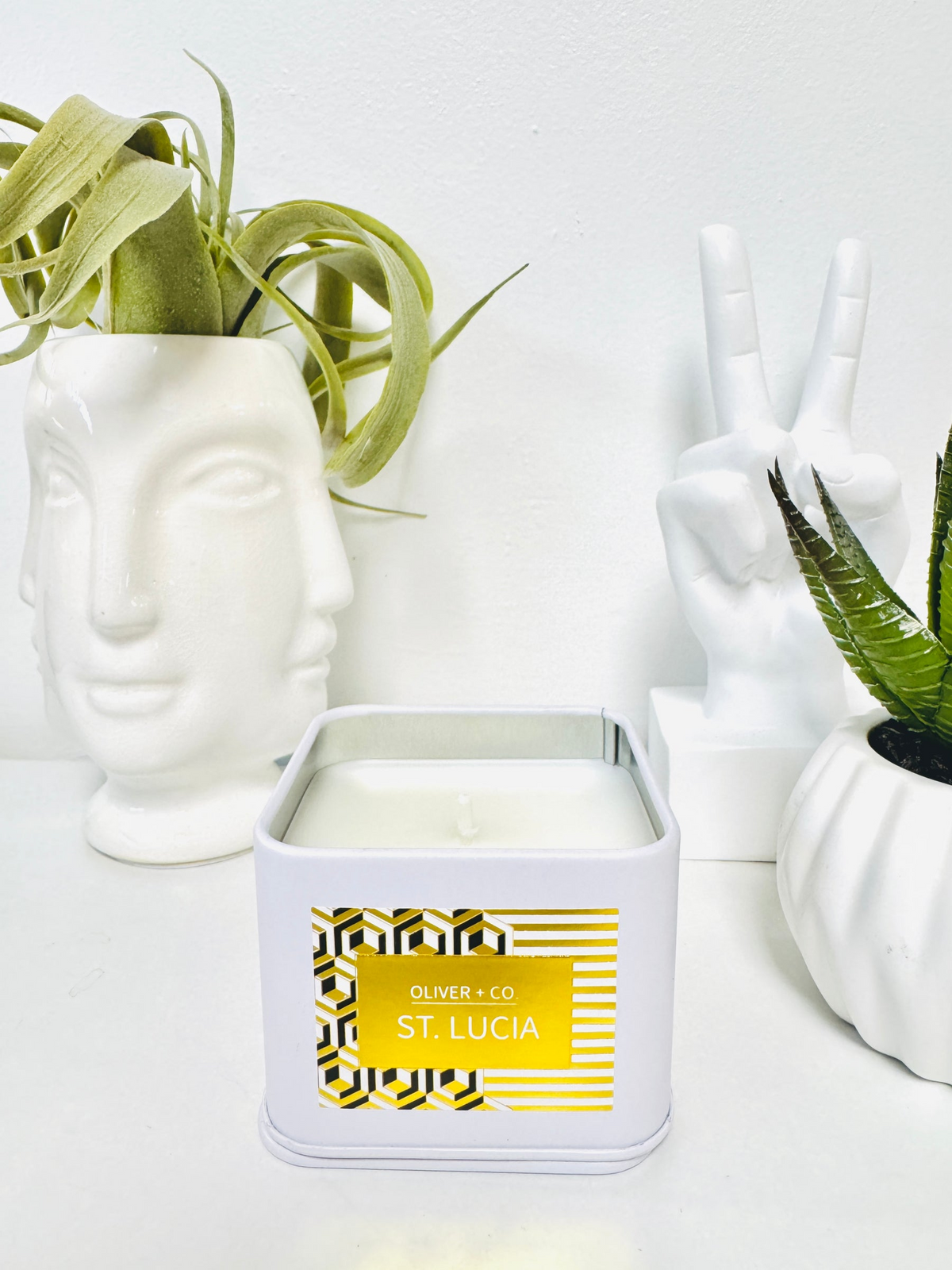 Travel Companion Candle in a white square tin labeled St. Lucia, next to white decorative objects.