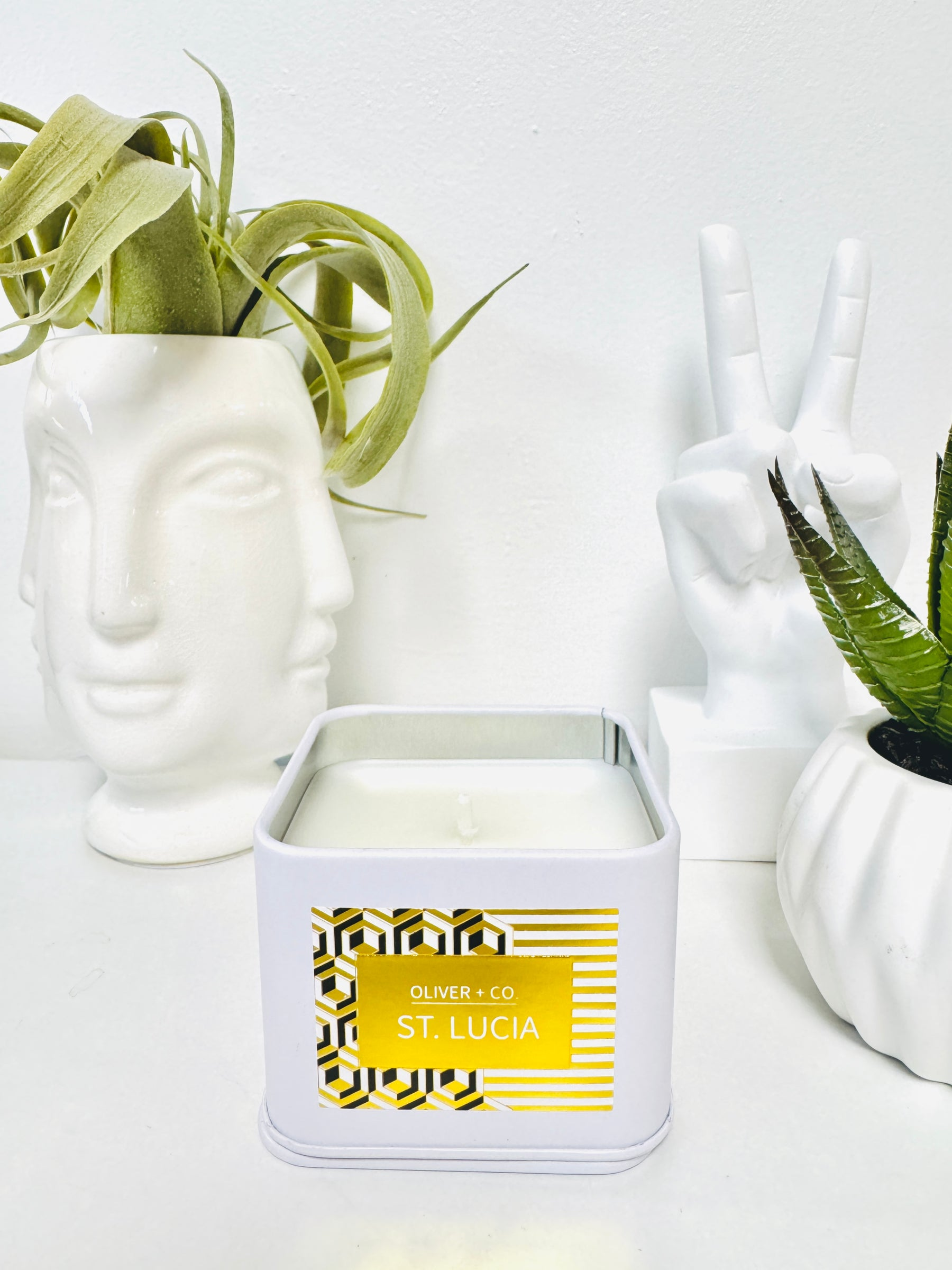 Travel Companion Candle in a white square tin labeled St. Lucia, next to white decorative objects.