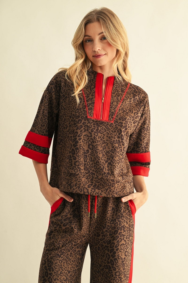 Woman wearing a brown leopard print faux suede top with red contrast stripes and a half-zip collar.