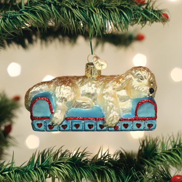 Sleepy Doodle Dog glass ornament showing a golden dog napping on a blue sofa with red heart details.