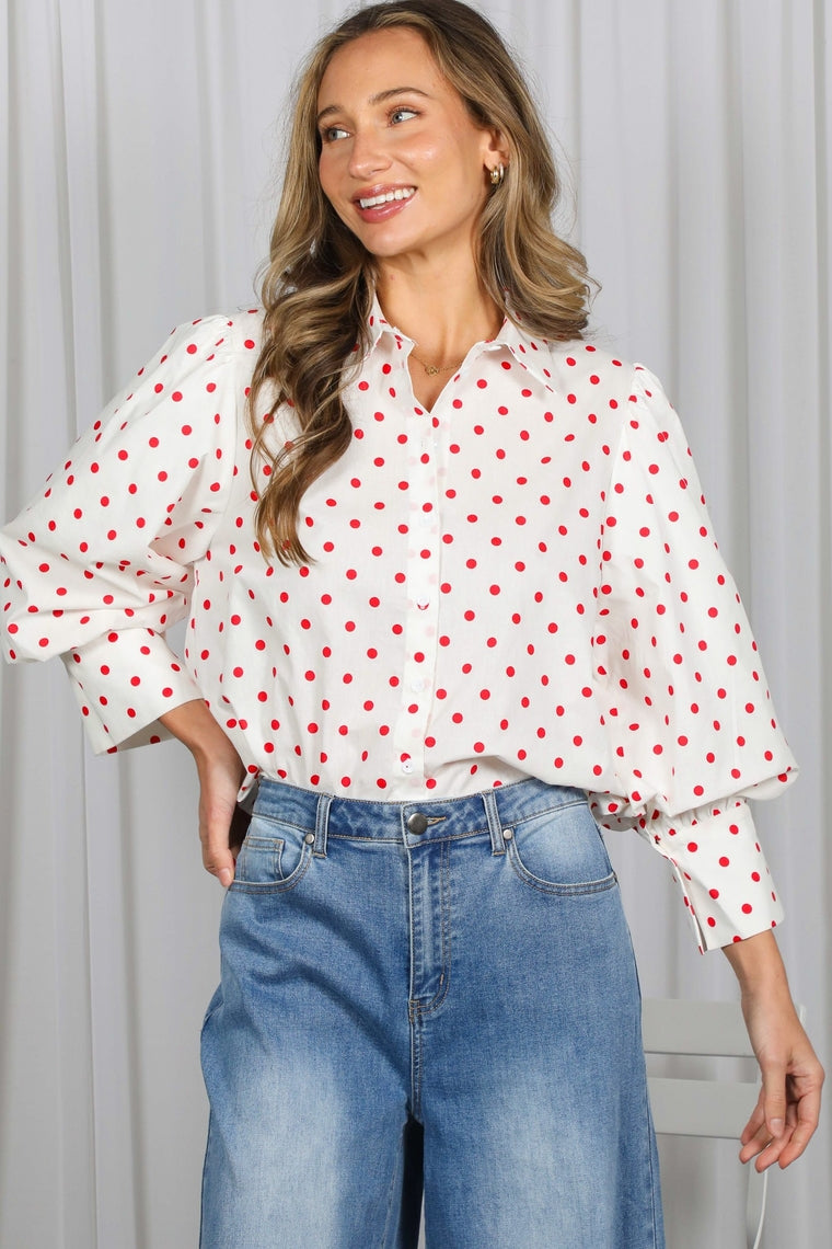Woman wearing a white button-front shirt with red polka dots and three-quarter puff sleeves.