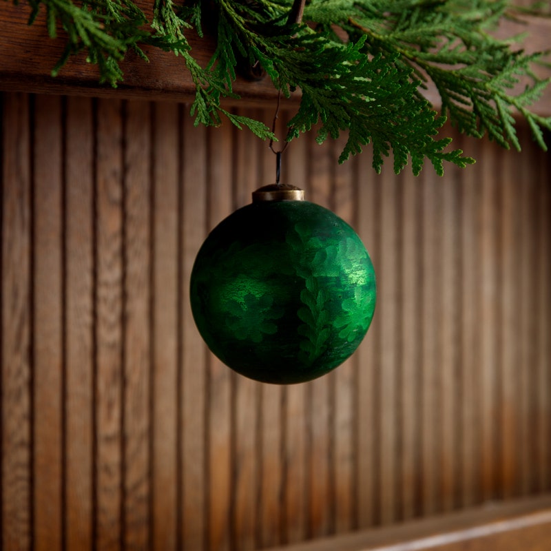 4-inch frosted green etched glass ball ornament hanging from a cedar branch.