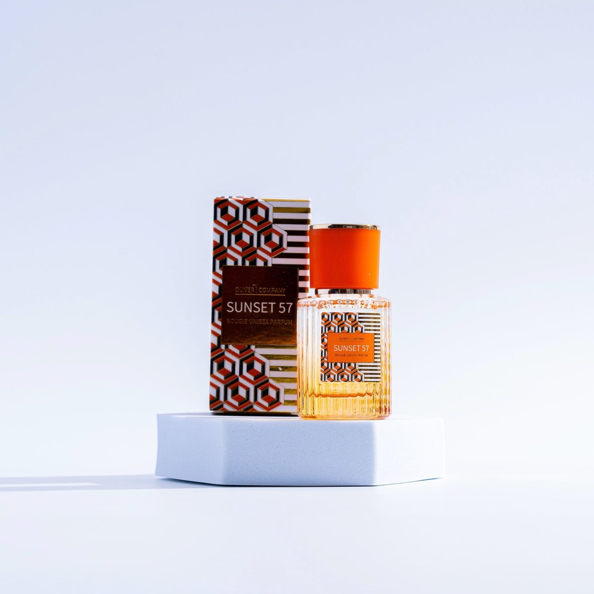 Sunset 57 Fragrance Mist bottle and patterned box on a white hexagonal pedestal.
