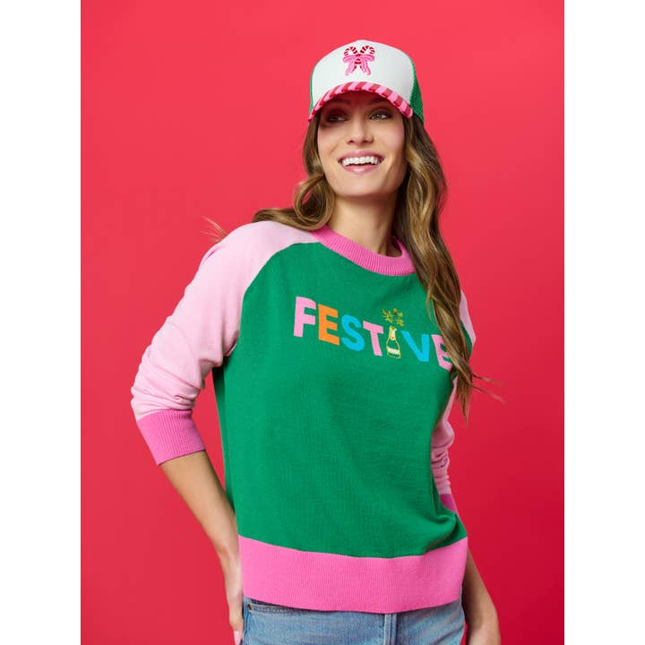 Woman wearing a white and green trucker hat with a candy cane bow graphic and striped brim.