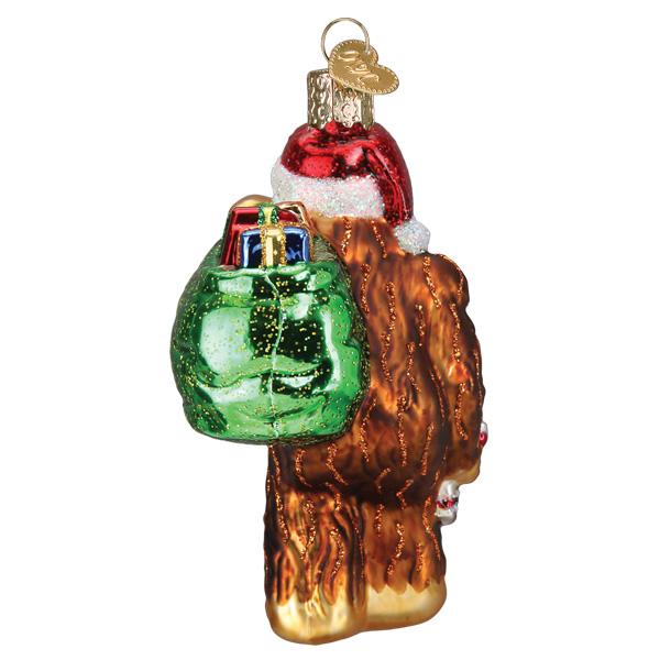 Back view of a Santa Sasquatch glass ornament carrying a green sack filled with colorful presents.