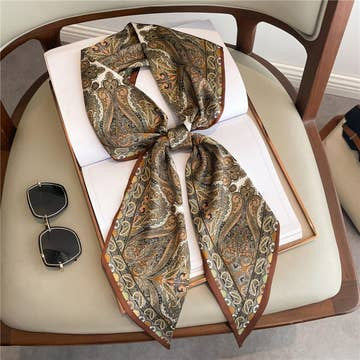 Double-layer paisley print head scarf tied in a bow on a book next to sunglasses.