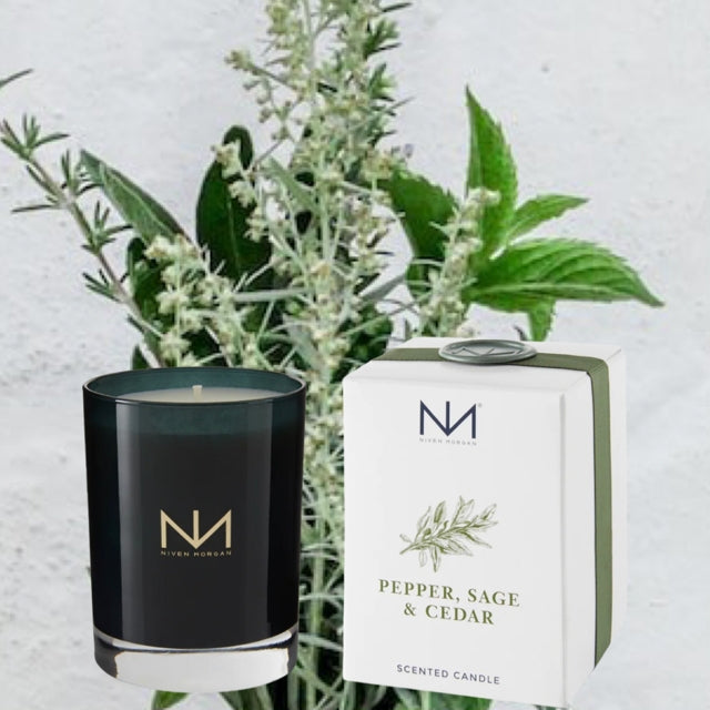 Niven Morgan Pepper, Sage & Cedar scented candle in a dark navy glass jar next to its white box.