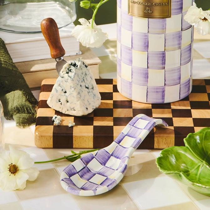 Curved enamel spoon rest with hand-painted purple check pattern on a white background.