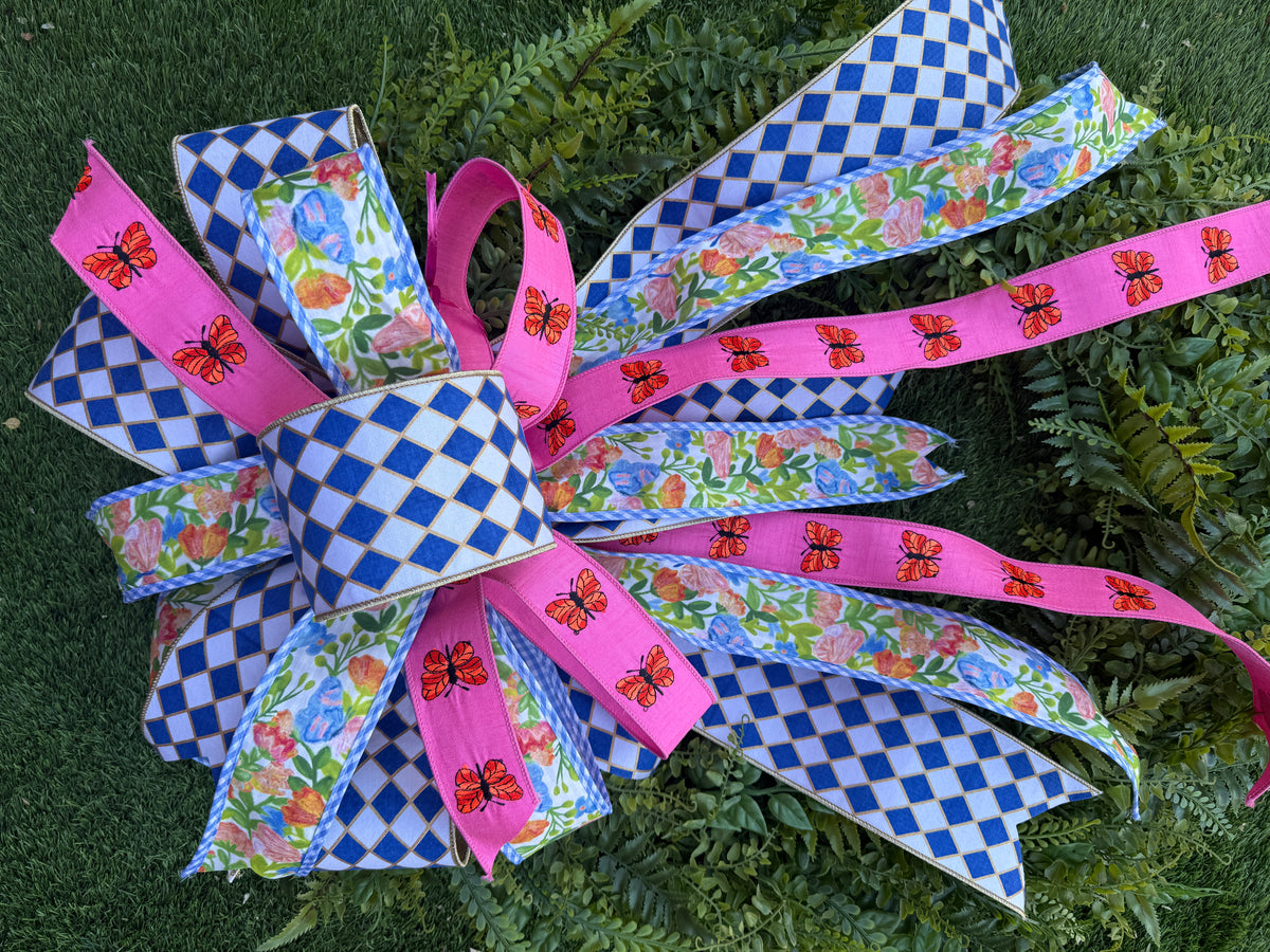 Checkered Butterfly Bow with blue diamond, floral, and pink butterfly ribbons on green foliage.
